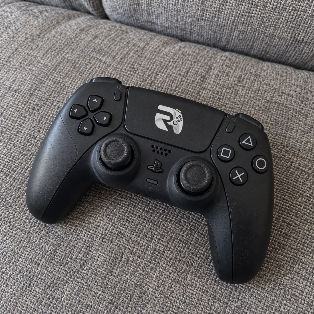 Controle preto com a marca Rise sobre um sofá cinza